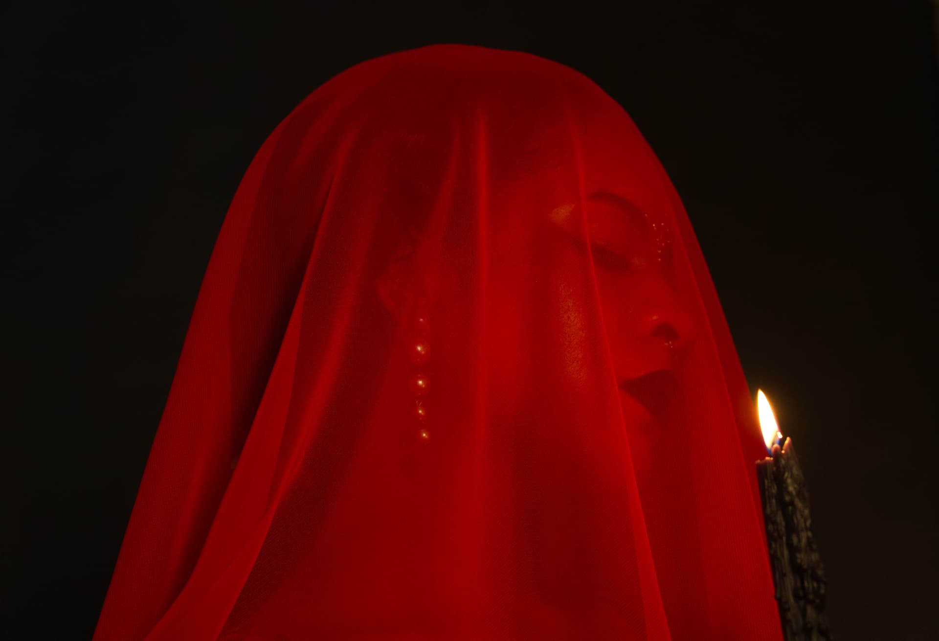 Model under a red veil beside a lit black candle